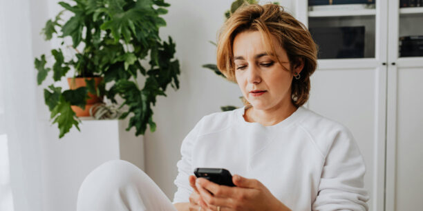 Woman in white sitting in a chair, scrolling GoFundMe on her phone